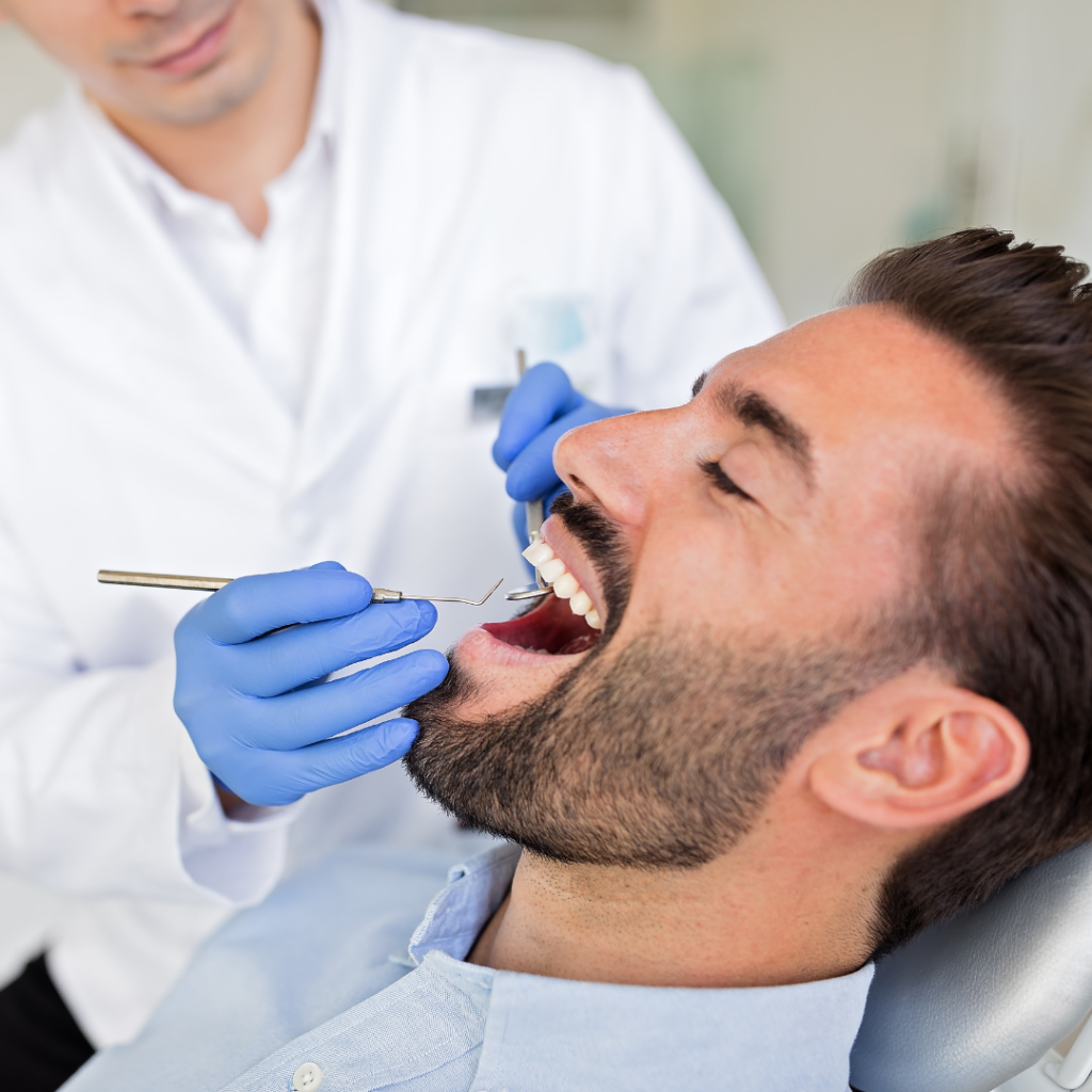 Hombre recibiendo un tratamiento dental mientras un dentista revisa sus dientes con herramientas dentales.