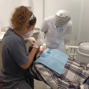 Una odontóloga realiza un procedimiento en un paciente que está recostado en un sillón dental. Otra persona con bata blanca está observando el procedimiento. El ambiente es limpio y profesional, con un logo de "García Ocaña" visible en la esquina inferior de la imagen.